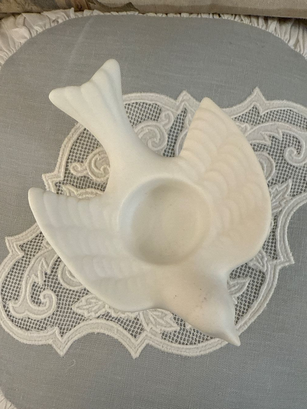 Bougeoir en biscuit blanc en forme d'hirondelle posé sur une nappe brodée, style romantique