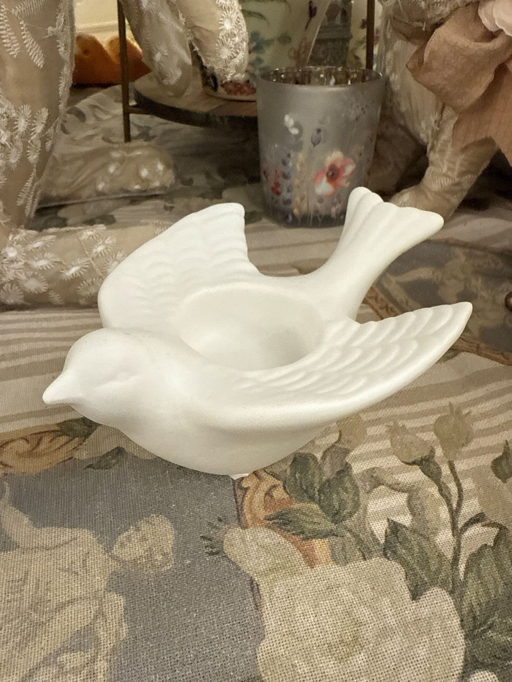 Bougeoir en biscuit blanc en forme d'hirondelle posé sur une nappe brodée, style romantique