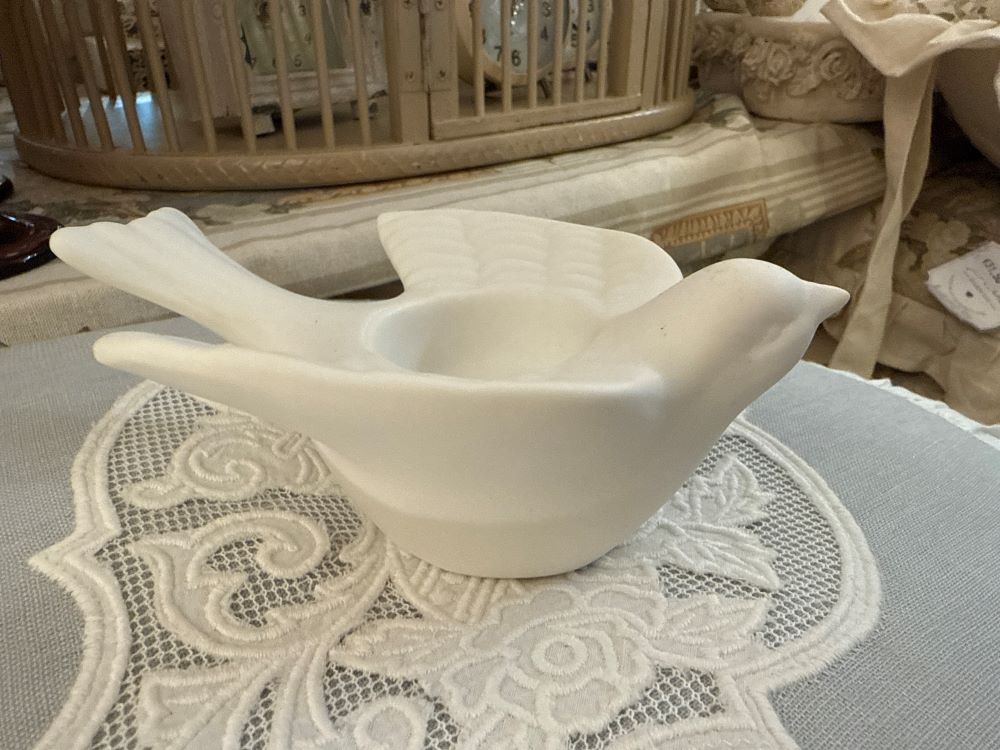 Bougeoir en biscuit blanc en forme d'hirondelle posé sur une nappe brodée, style romantique
