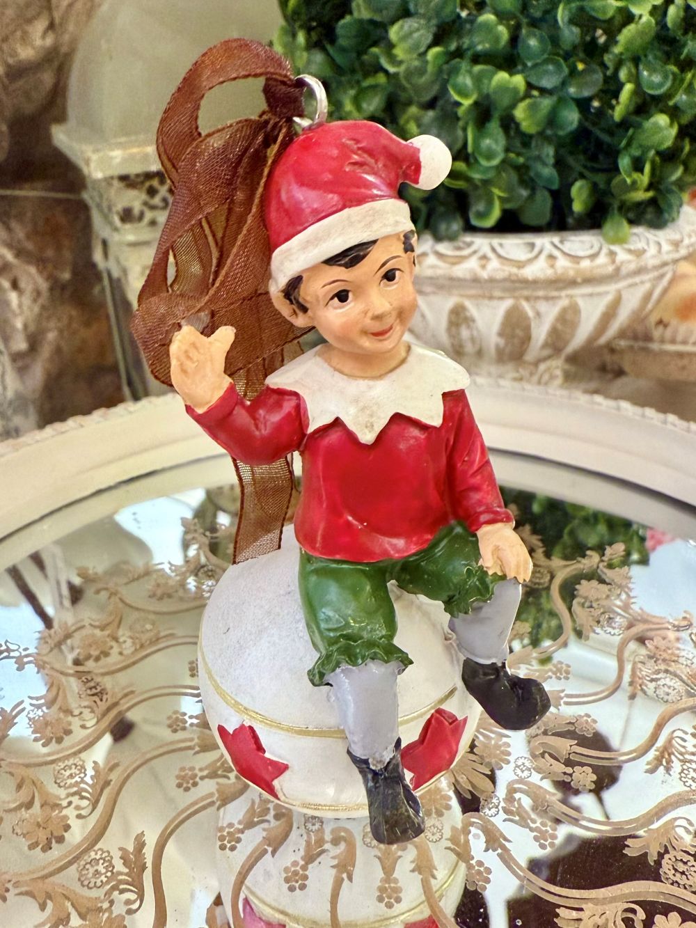 Suspension de Noël représentant un lutin rouge et vert assis sur une boule blanche décorée d’étoiles rouges, à suspendre dans le sapin, style féérique et romantique