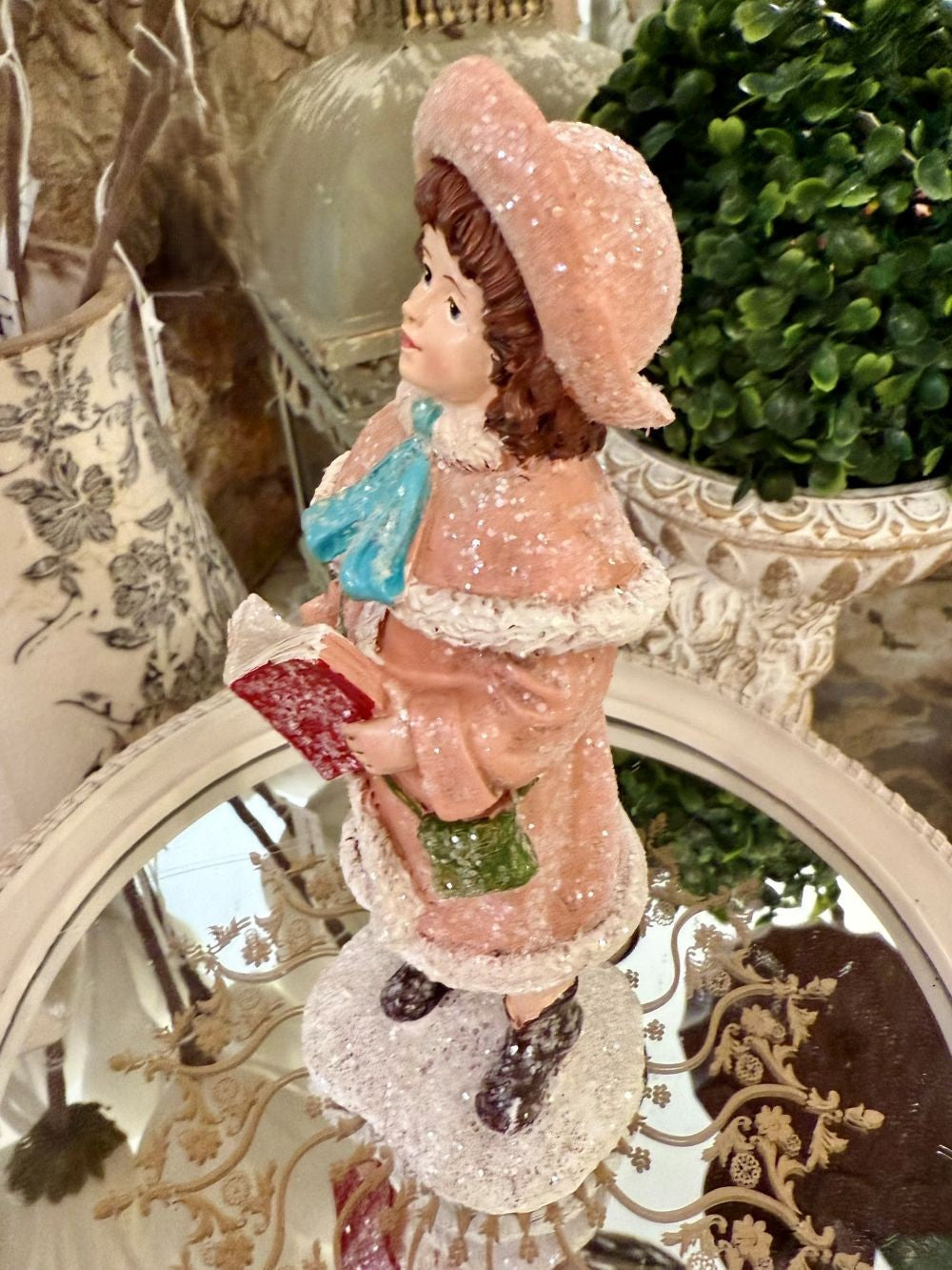 Figurine de Noël représentant une petite chanteuse en manteau rose et bonnet assorti, dans un style victorien romantique, sur fond de décoration shabby chic