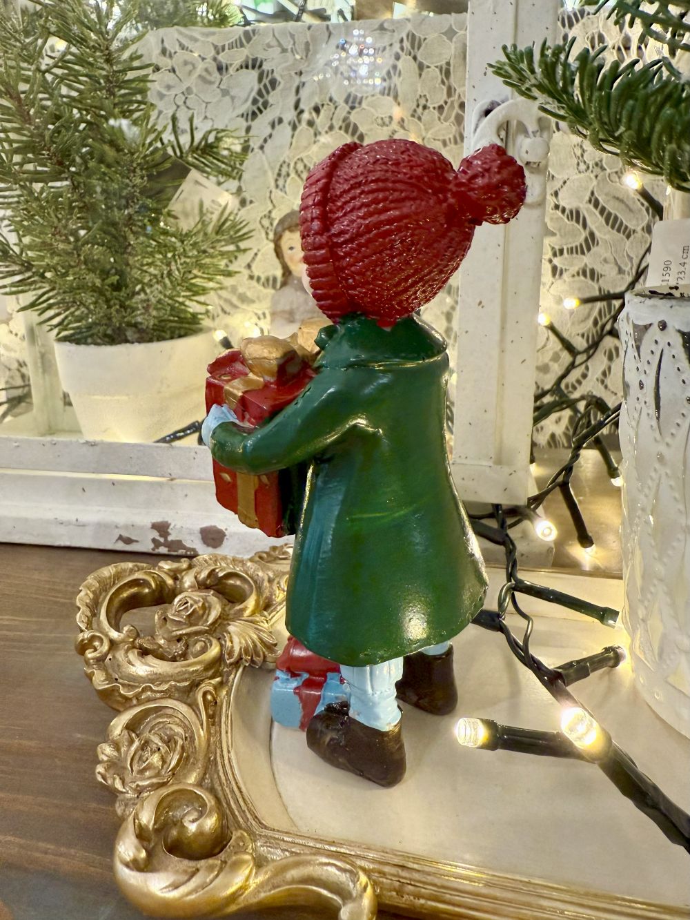 Figurine de Noël représentant une petite fille en manteau vert et bonnet rouge tenant des cadeaux, style vintage et ambiance romantique, décoration poétique pour fêtes de fin d’année