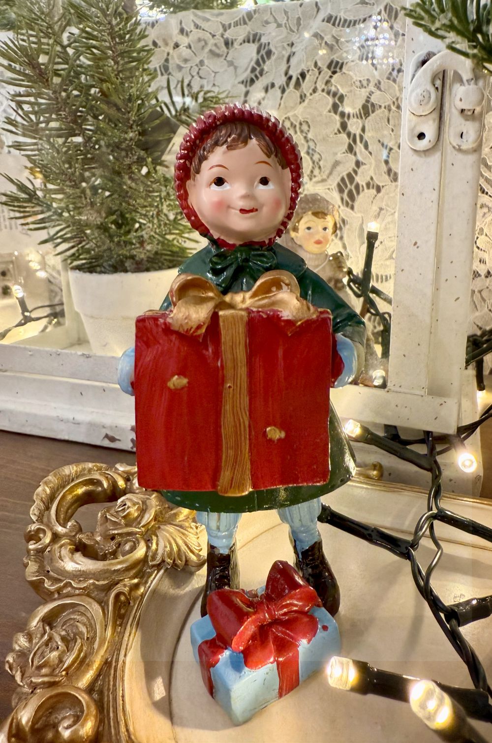 Figurine de Noël représentant une petite fille en manteau vert et bonnet rouge tenant des cadeaux, style vintage et ambiance romantique, décoration poétique pour fêtes de fin d’année