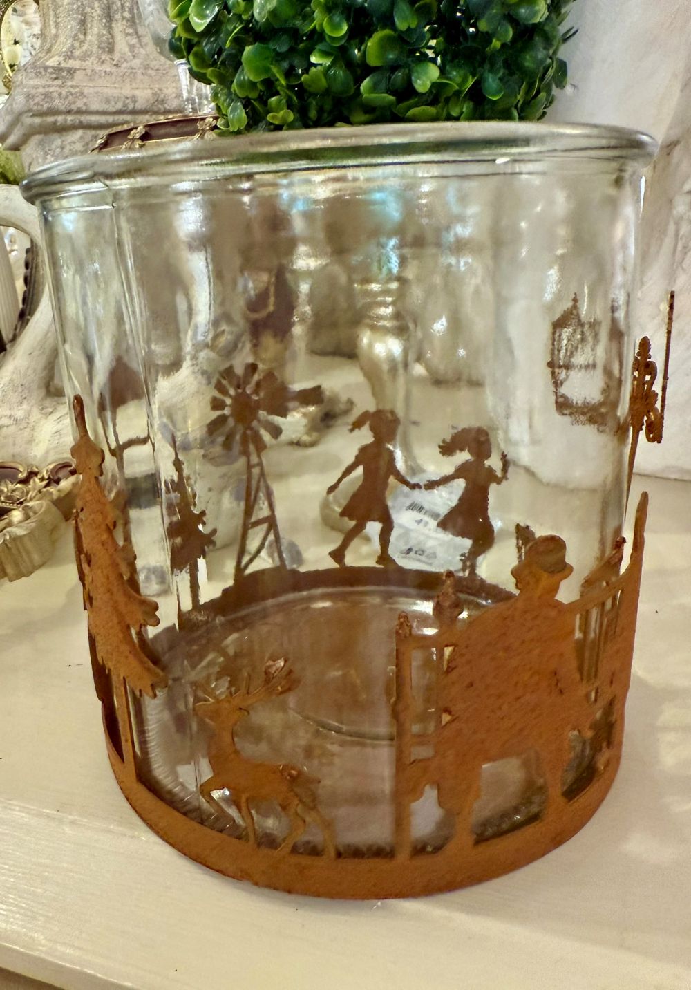 Photophore en verre 15x15 cm avec décor en métal rouille représentant une scène de village d’hiver, enfants, arbres et animaux, style romantique et féérique