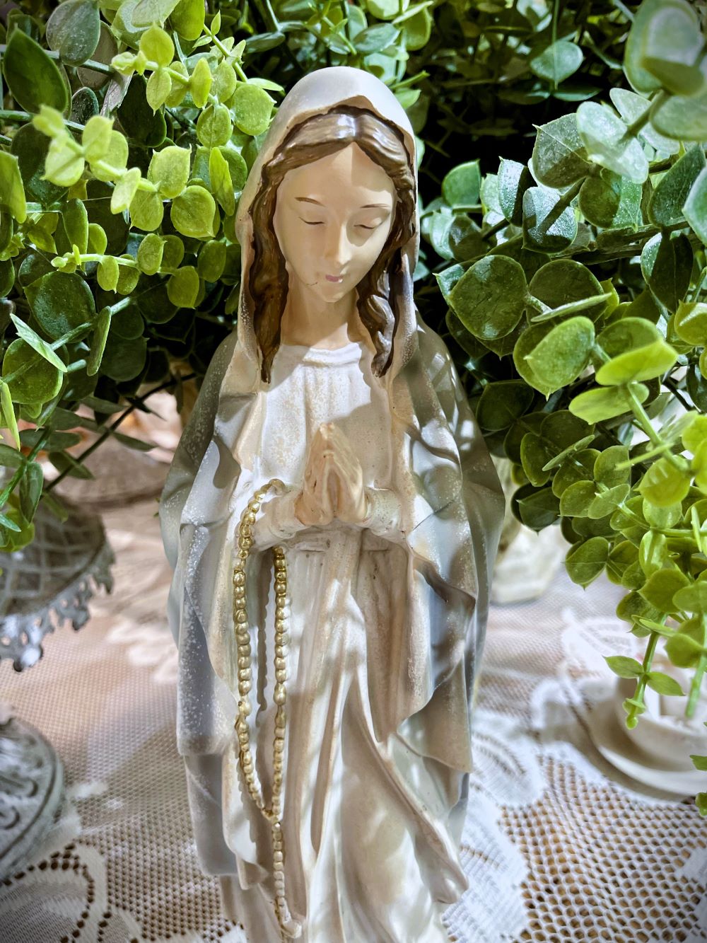 Statuette décorative de la Vierge Marie en prière tenant un chapelet doré, finitions nacrées blanc cassé, détails roses à la base, style romantique et shabby chic, ambiance spirituelle et poétique