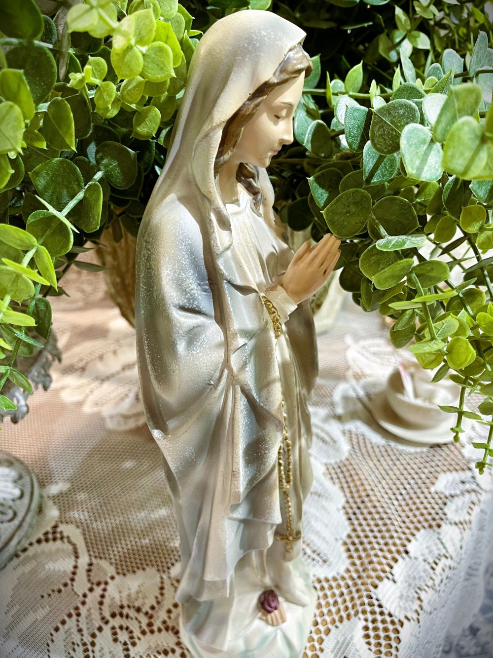 Statuette décorative de la Vierge Marie en prière tenant un chapelet doré, finitions nacrées blanc cassé, détails roses à la base, style romantique et shabby chic, ambiance spirituelle et poétique