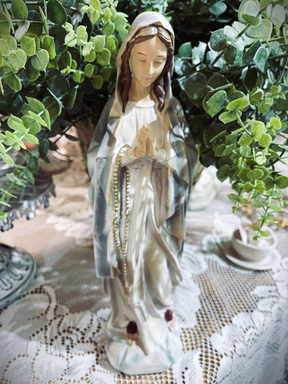 Statuette décorative de la Vierge Marie en prière tenant un chapelet doré, finitions nacrées blanc cassé, détails roses à la base, style romantique et shabby chic, ambiance spirituelle et poétique