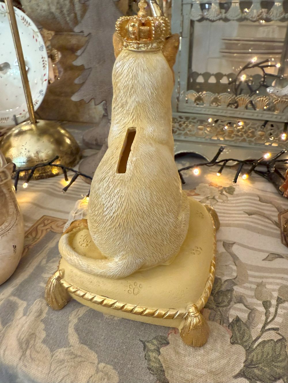Tirelire décorative en forme de chat couronné, couleurs beige, doré et marron, style shabby chic romantique et poétique, posée sur un coussin élégant