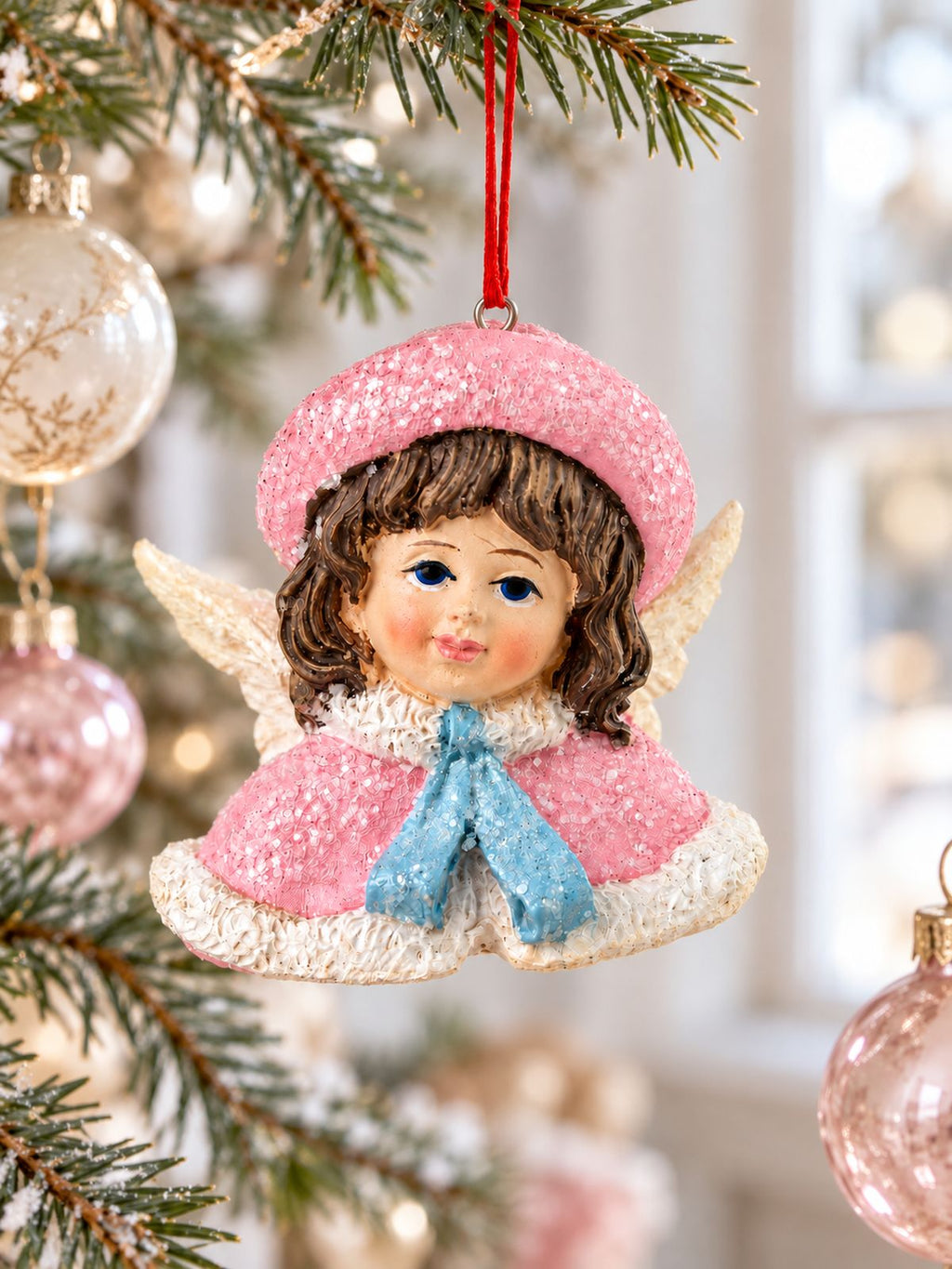 Ange Poupée Victorienne rose suspendu à une branche de sapin, parmi des boules de Noël blanches et roses.
