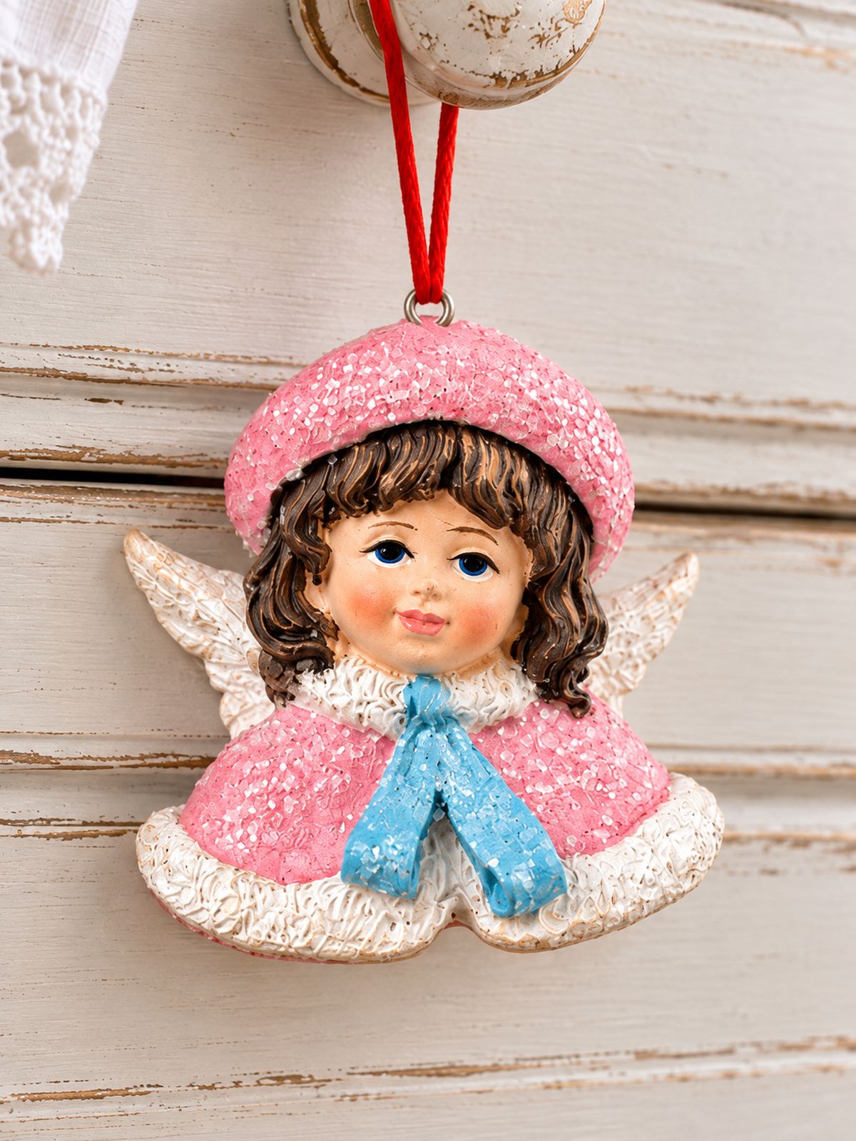 Gros plan de la figurine Ange Poupée Victorienne rose et bleu suspendue au bouton d’une commode blanche patinée.