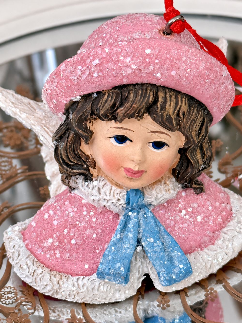 Détail du visage peint de l’Ange Poupée Victorienne, de son bonnet rose et de son ruban bleu pailleté.