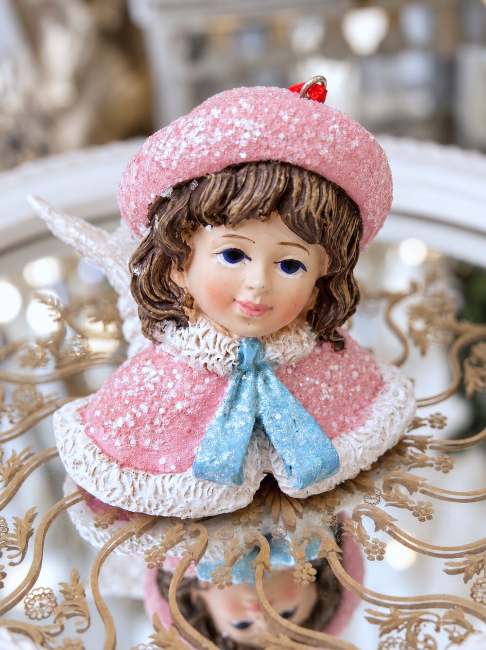 Ange Poupée Victorienne rose et bleu posé sur un plateau miroir à motifs dorés.