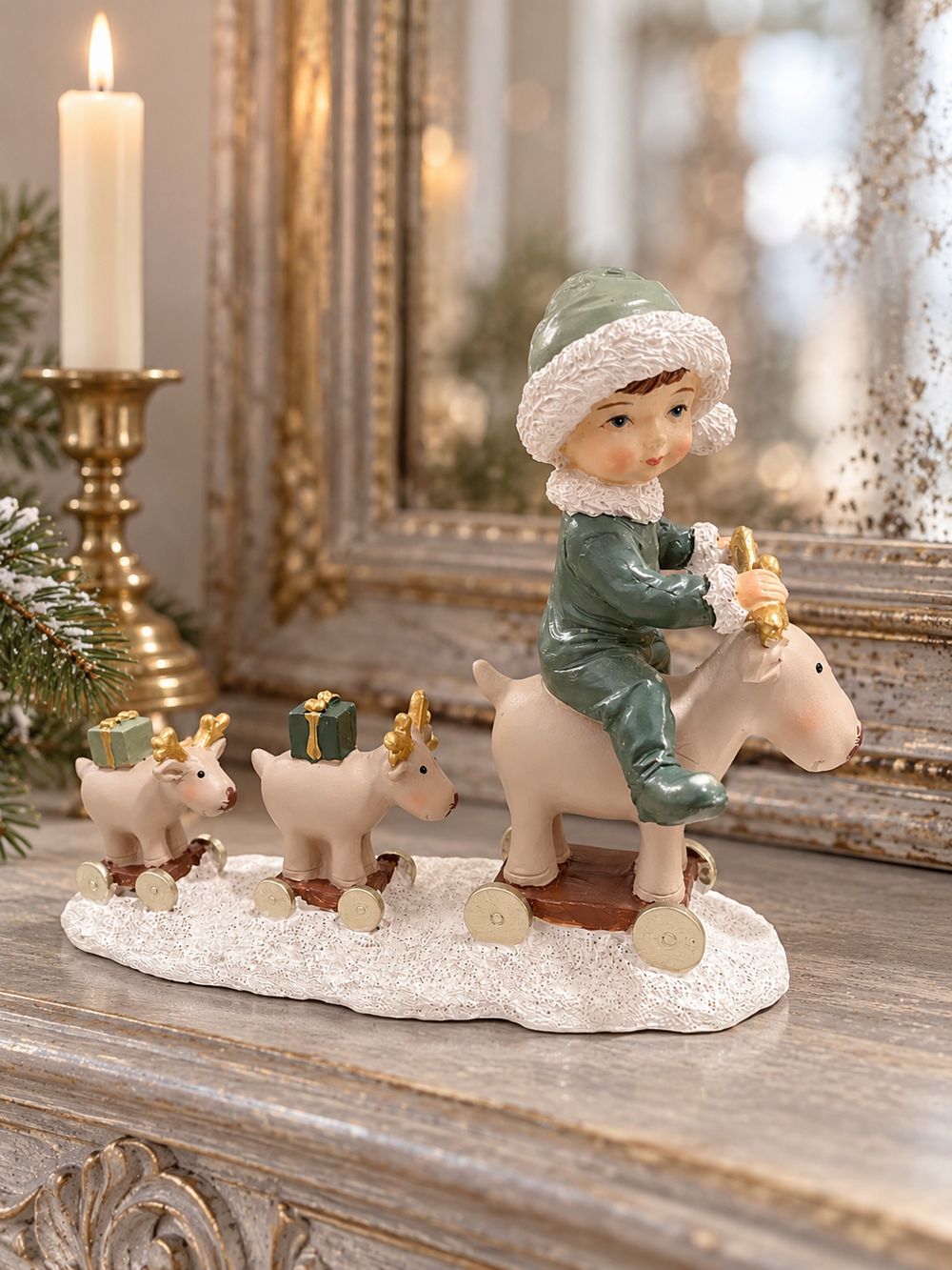 Statuette Balade des Petits Rennes sur une console patinée, devant un miroir ancien, près d’un bougeoir et d’une branche de sapin.