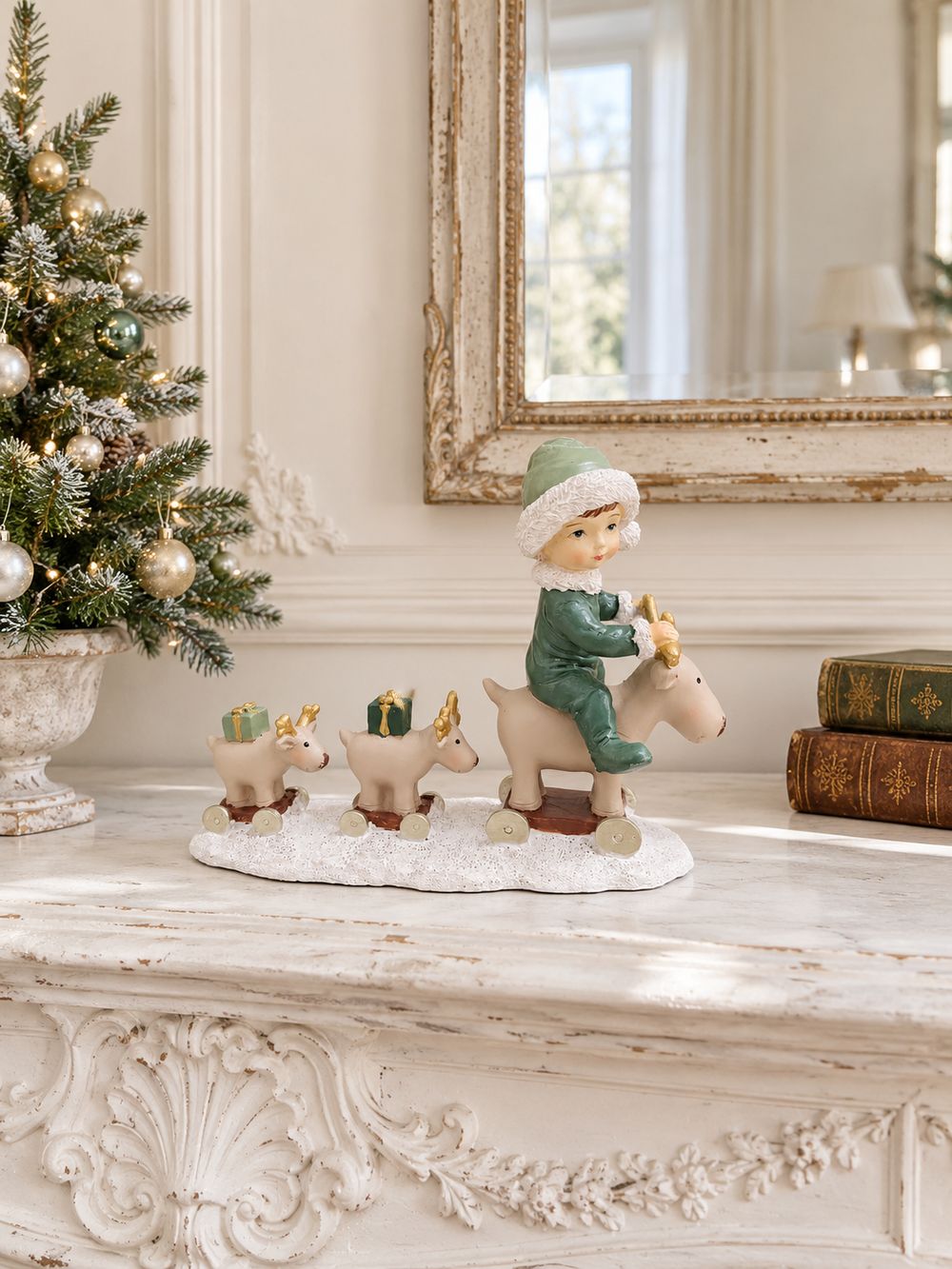 Statuette Balade des Petits Rennes sur un manteau de cheminée blanc patiné, entre un petit sapin décoré et des livres anciens.