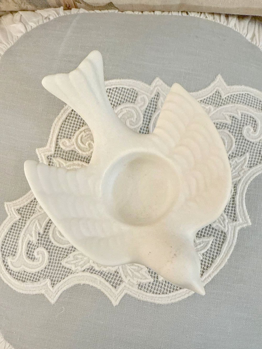 Bougeoir en biscuit blanc en forme d'hirondelle posé sur une nappe brodée, style romantique