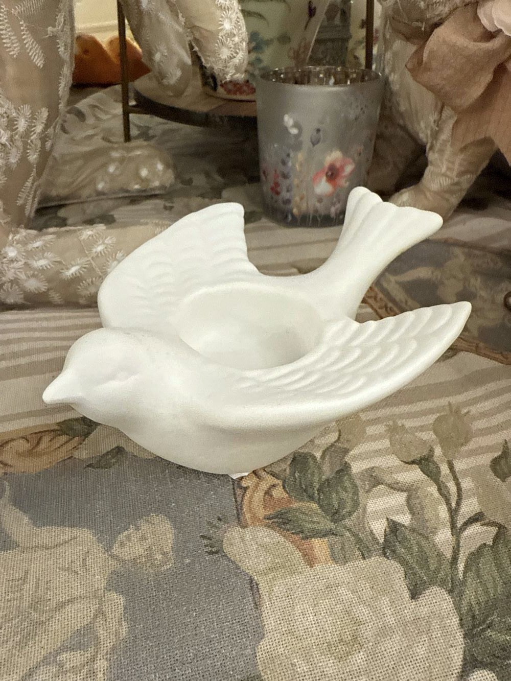 Bougeoir en biscuit blanc en forme d'hirondelle posé sur une nappe brodée, style romantique