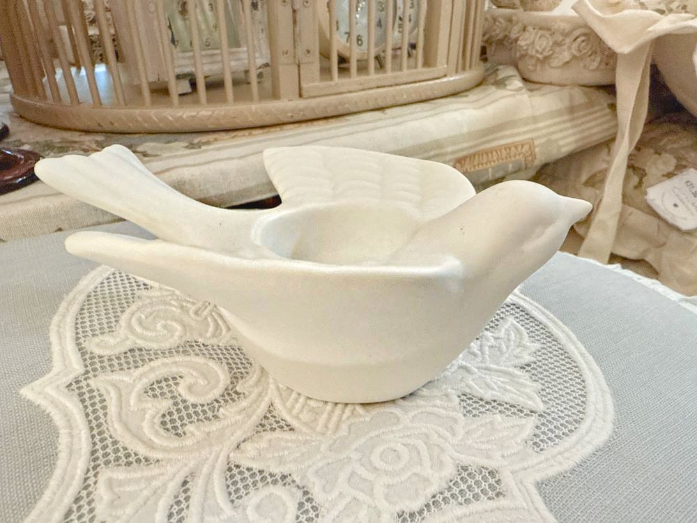 Bougeoir en biscuit blanc en forme d'hirondelle posé sur une nappe brodée, style romantique