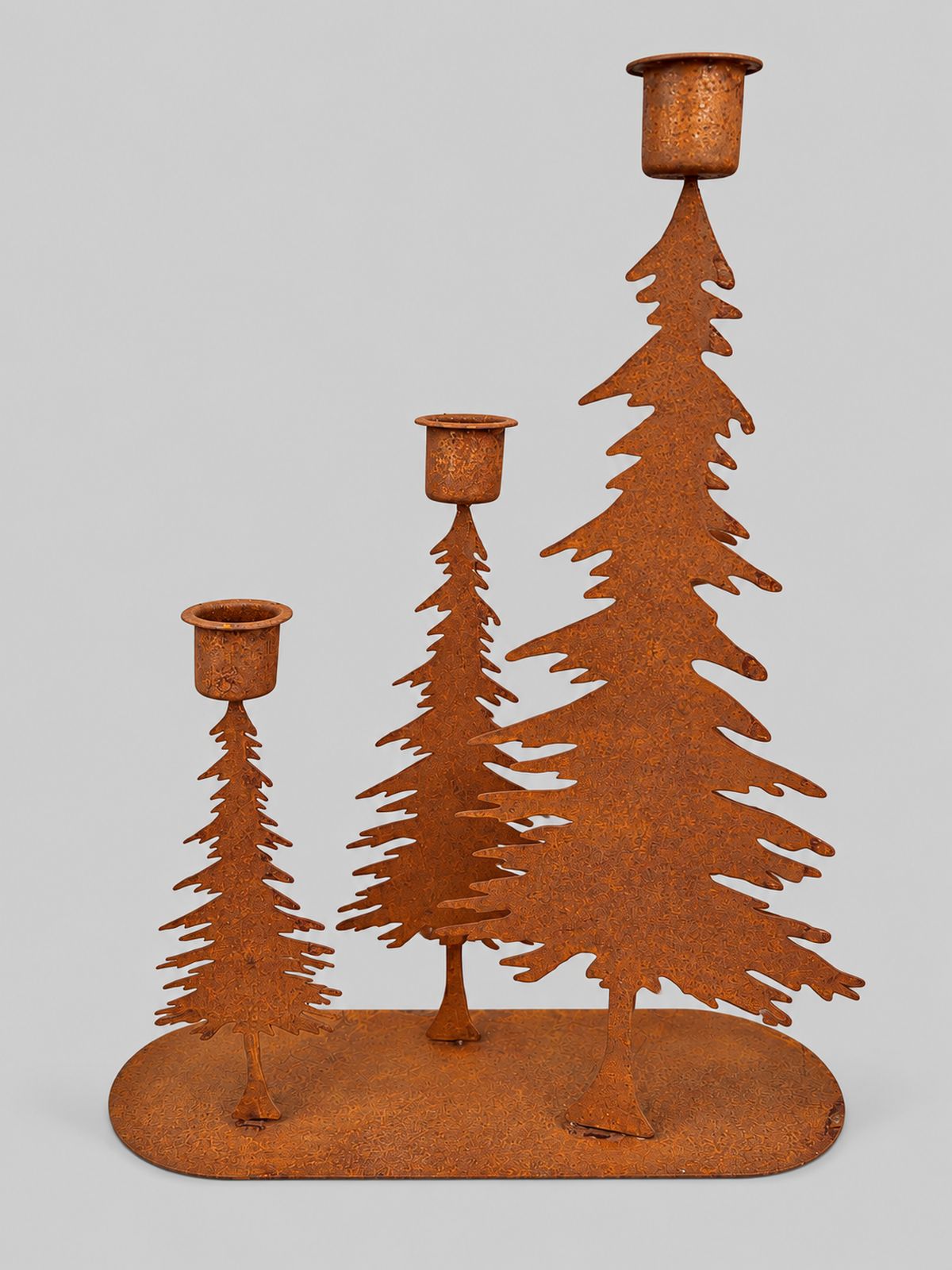 Bougeoir à trois sapins en métal patiné rouille, sans bougies, sur fond gris clair.