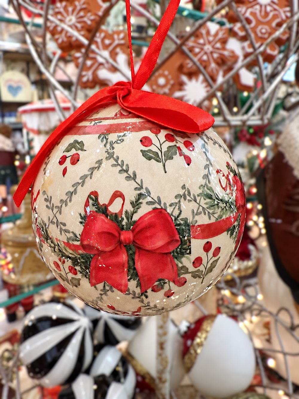 Détail du motif de nœud rouge et de feuillages sur la boule de Noël crème.