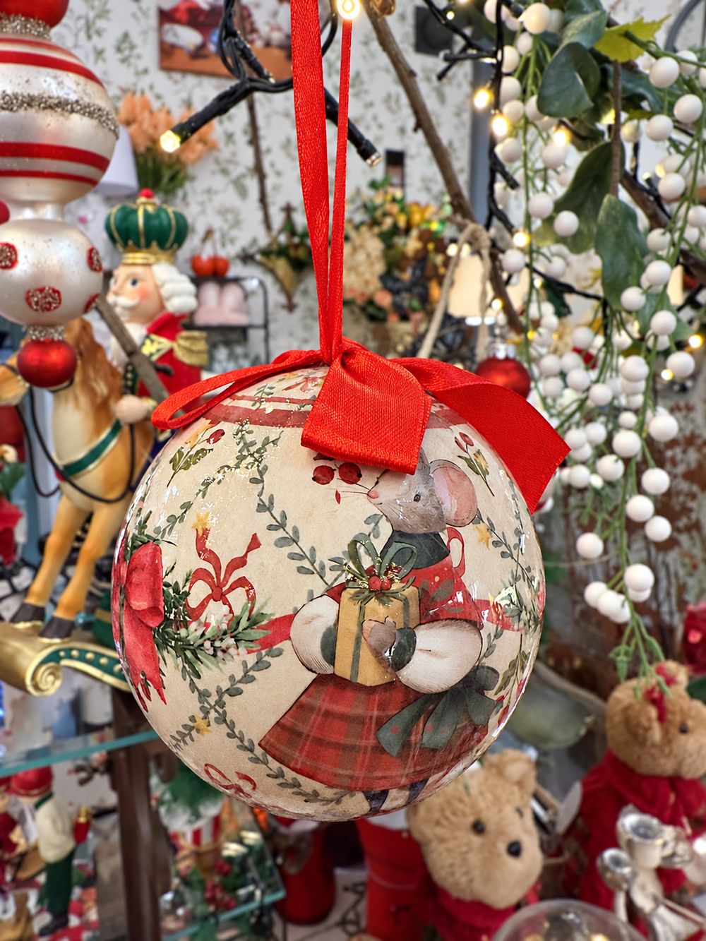 Boule de Noël au motif de souris portant un cadeau, suspendue par un ruban rouge, vue de détail.
