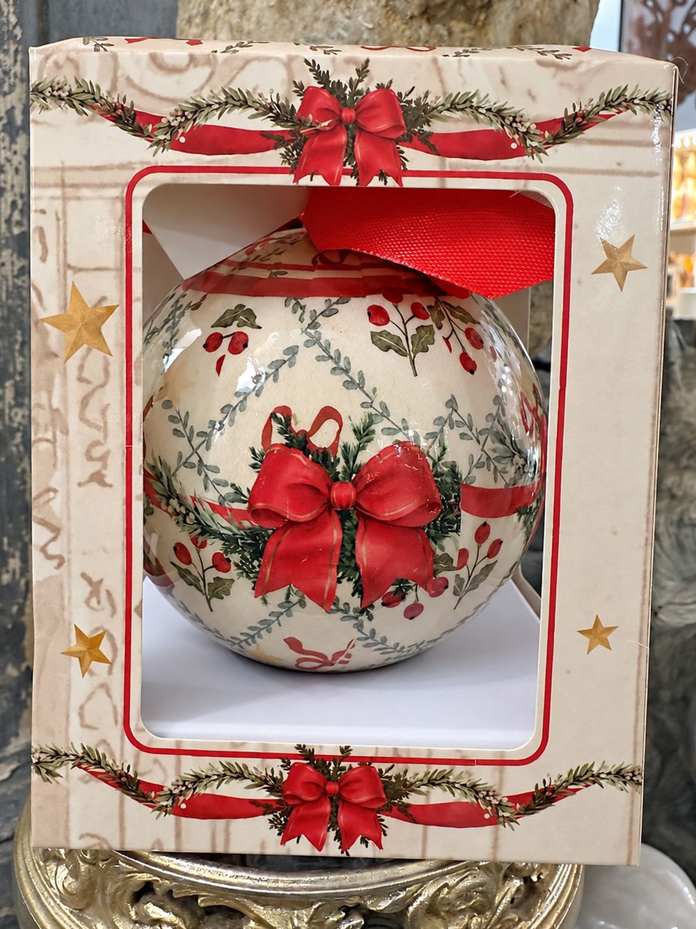 Boule de Noël dans son coffret, vue du motif de nœud rouge et de feuillages.