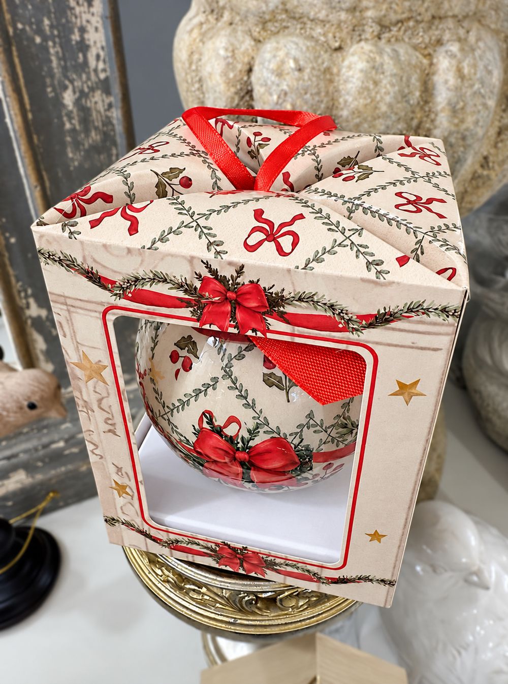 Coffret de la boule de Noël vu de dessus, avec motifs végétaux et poignée en ruban rouge.