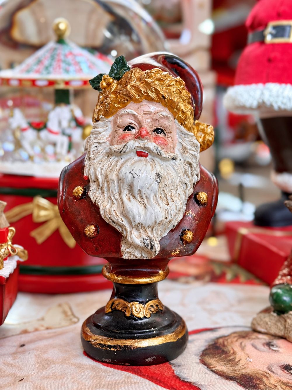 Vue de face du buste du Père Noël rouge et doré sur son socle noir.