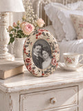 Cadre photo fleuri avec un portrait de couple de style ancien, posé sur un chevet blanc près d’une tasse.