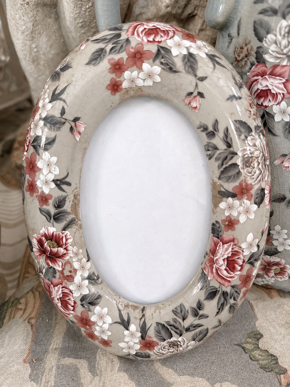 Vue de face du cadre photo bucolique ovale, avec ses fleurs rouges et blanches et sa finition patinée.