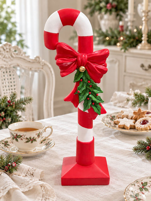 Canne à sucre rouge et blanche sur une table de Noël, accompagnée d’une tasse en porcelaine et de biscuits.