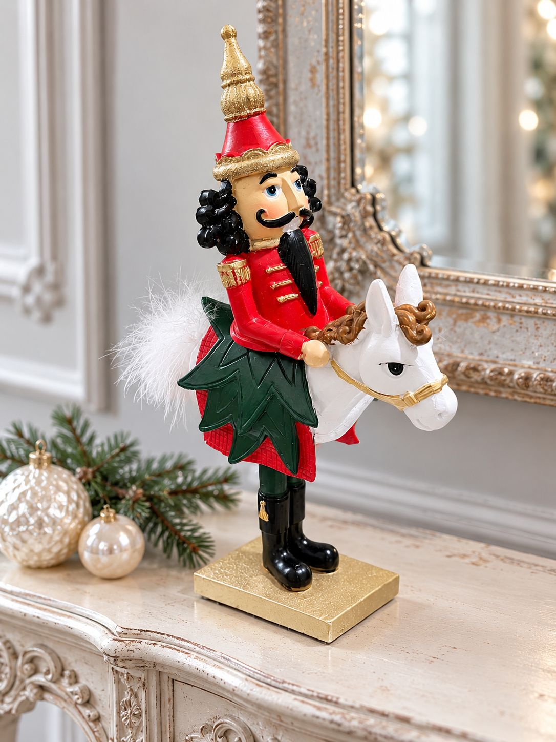 Casse-Noisette Cavalier Royal sur une console patinée devant un miroir ancien, accompagné de boules de Noël nacrées.