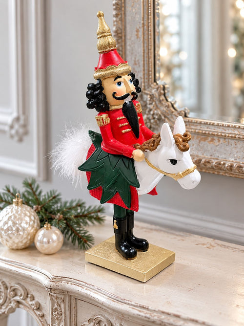 Casse-Noisette Cavalier Royal sur une console patinée devant un miroir ancien, accompagné de boules de Noël nacrées.