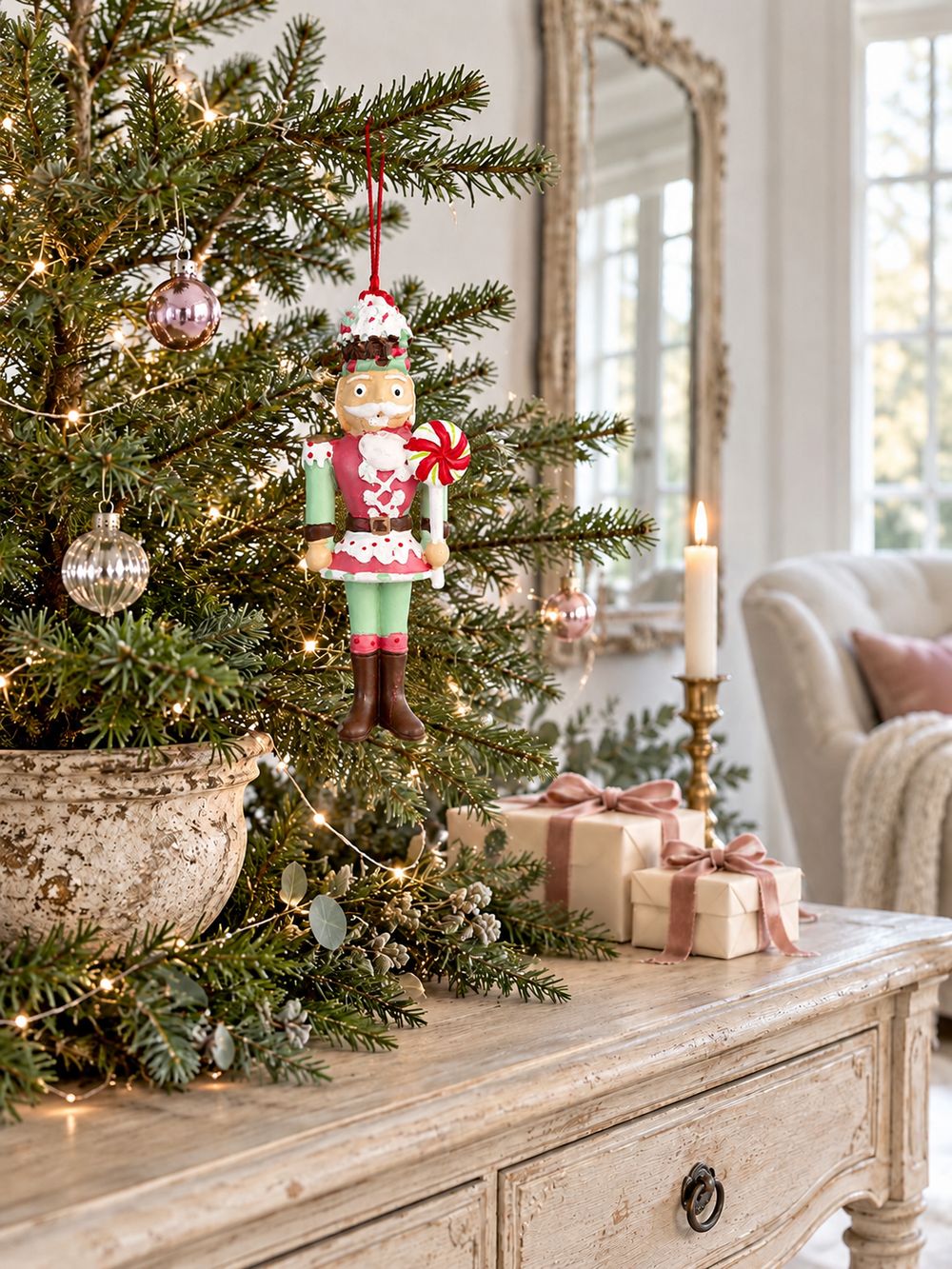 Casse-noisette suspendu verticalement dans un petit sapin sur une console patinée, avec des cadeaux et un bougeoir dans un salon lumineux.