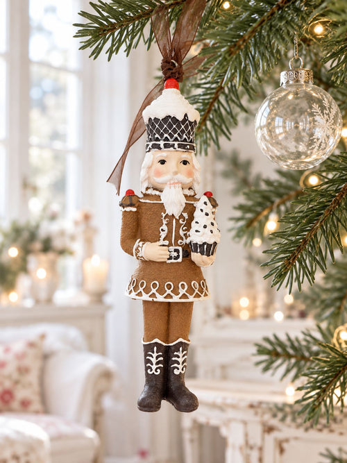 Casse-noisette Cupcake suspendu à une branche de sapin près d’une boule en verre, dans un intérieur lumineux.