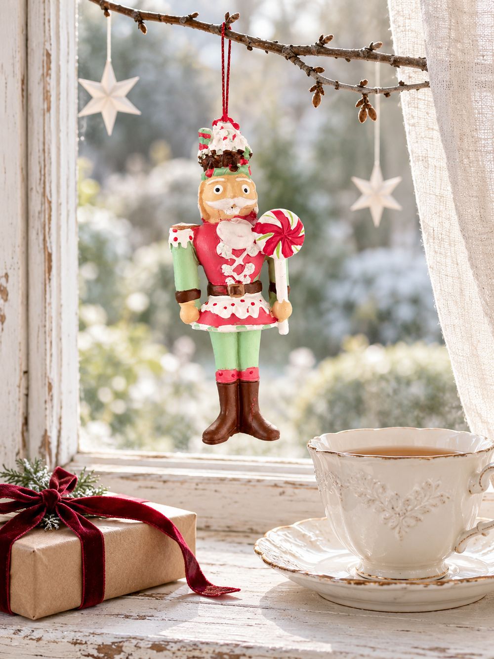Casse-noisette suspendu à une branche devant une fenêtre ancienne, au-dessus d’une tasse de thé et d’un cadeau.