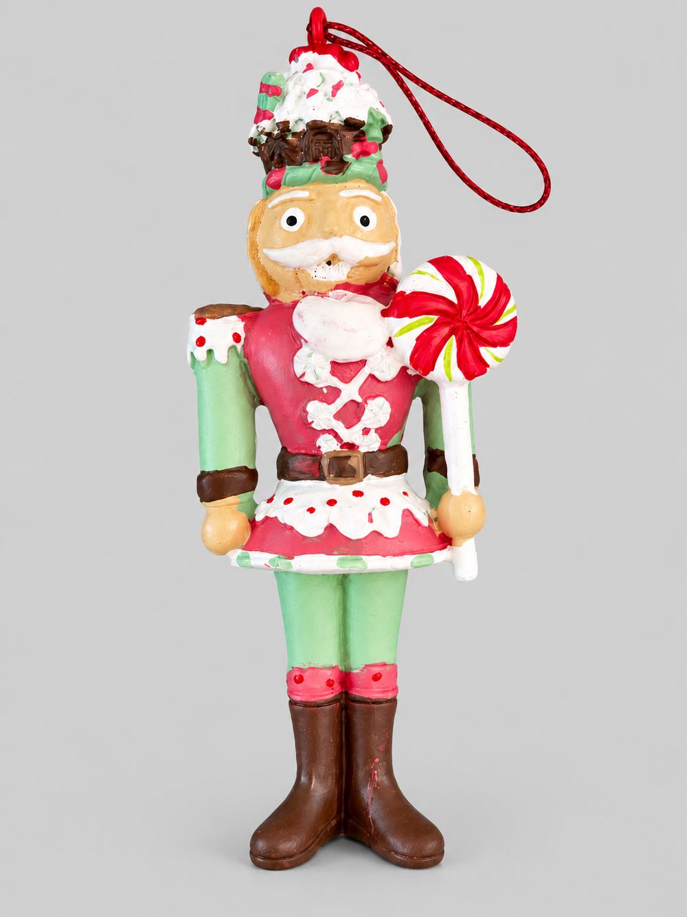 Casse-noisette à suspendre rouge et vert, tenant une sucette, présenté sur fond gris clair.