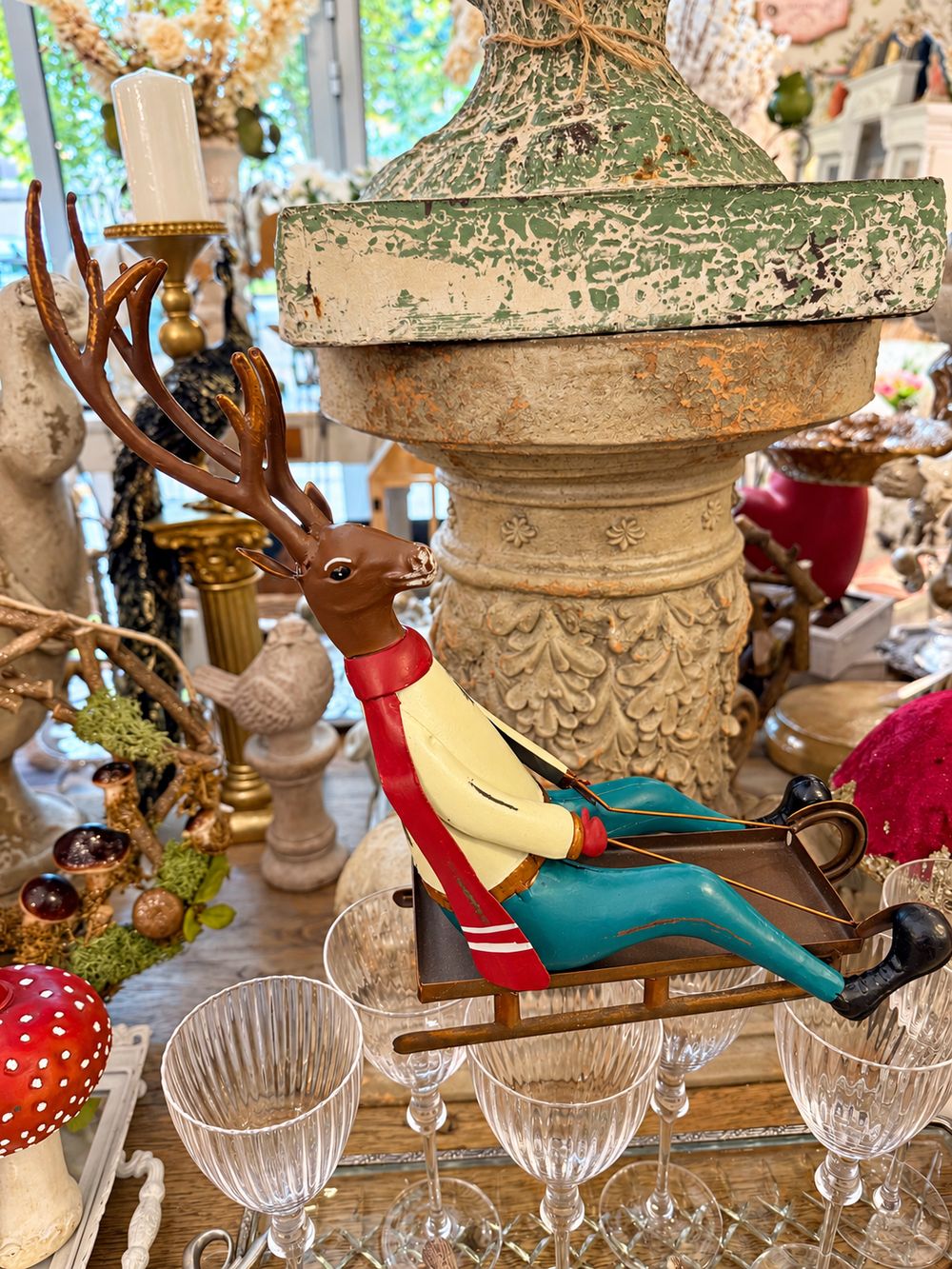 Cerf décoratif assis sur une luge, aux tons marron, rouge, jaune et bleu turquoise, style vintage et fantaisiste pour une décoration de Noël.