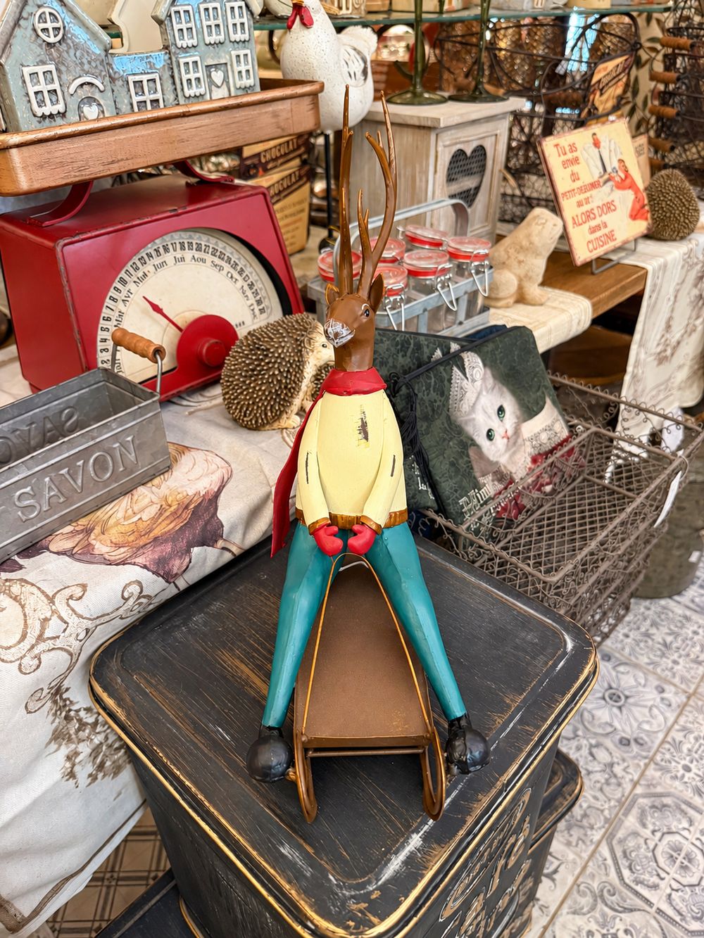 Cerf décoratif assis sur une luge, aux tons marron, rouge, jaune et bleu turquoise, style vintage et fantaisiste pour une décoration de Noël.