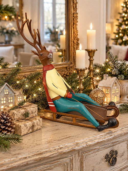 Cerf décoratif assis sur une luge, aux tons marron, rouge, jaune et bleu turquoise, style vintage et fantaisiste pour une décoration de Noël.