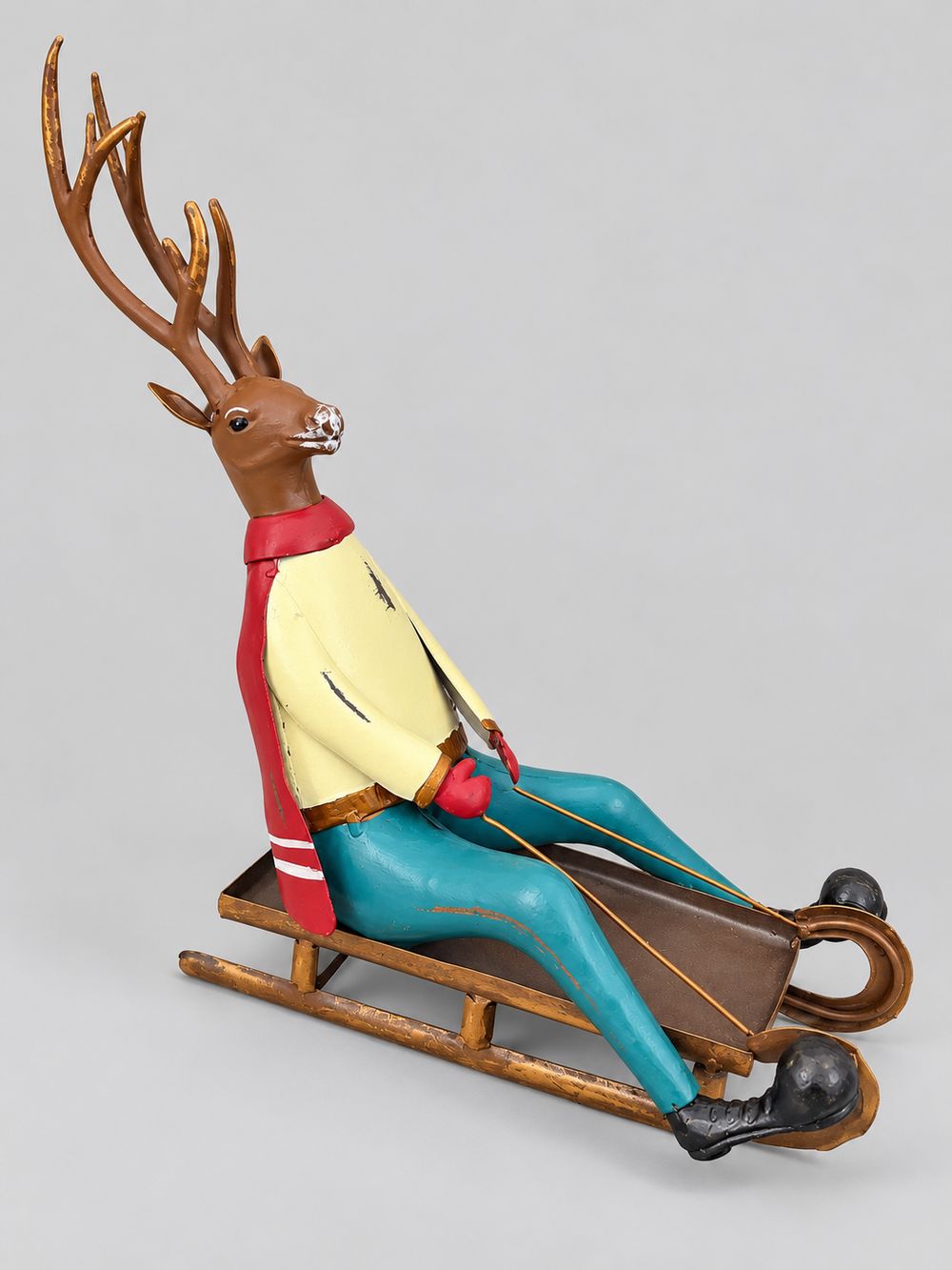 Cerf décoratif assis sur une luge, aux tons marron, rouge, jaune et bleu turquoise, style vintage et fantaisiste pour une décoration de Noël.
