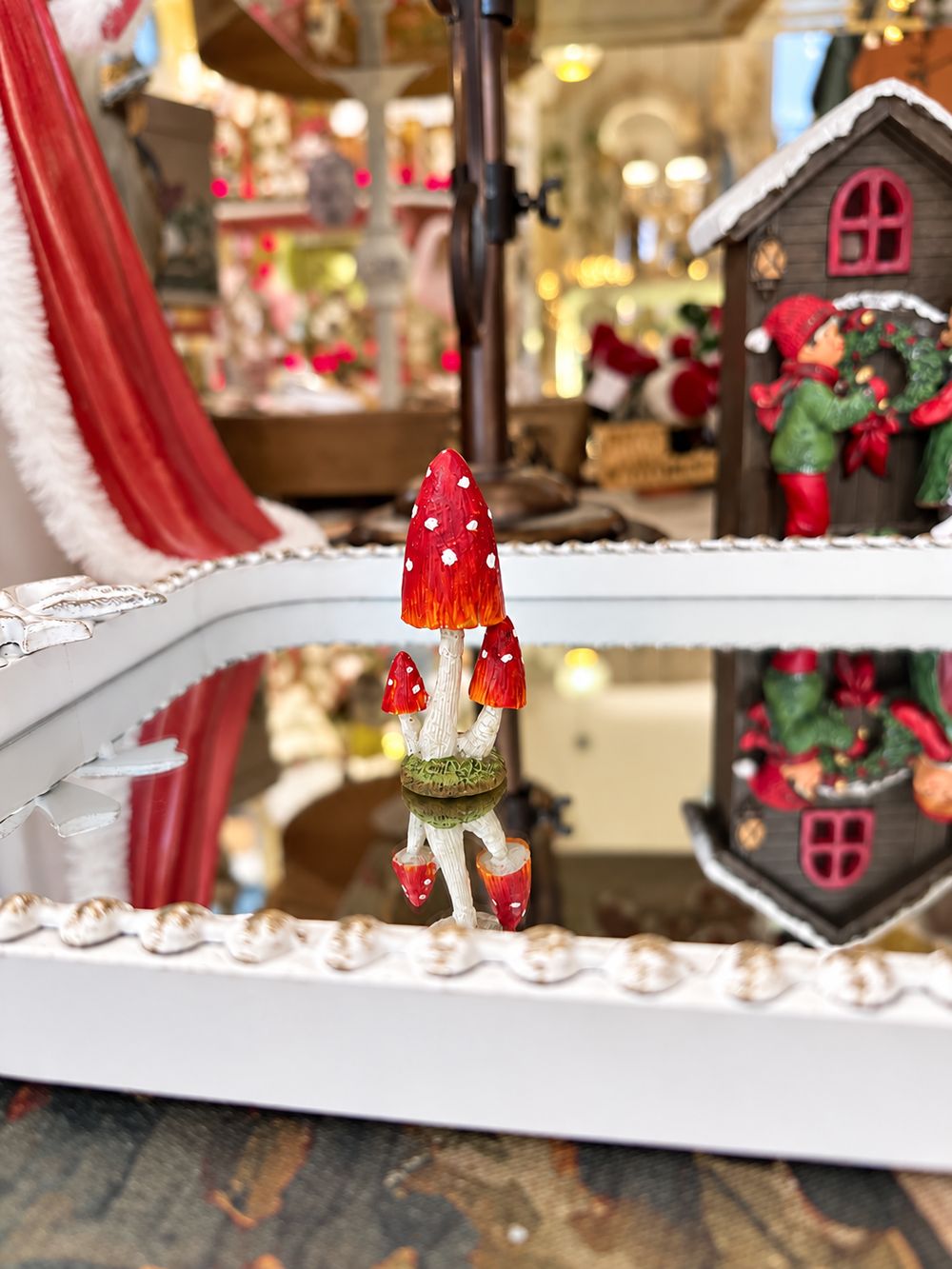 Petit champignon décoratif miniature rouge à pois blancs sur pied clair et base verte, pour décor féérique, village de Noël ou scène de sous-bois.