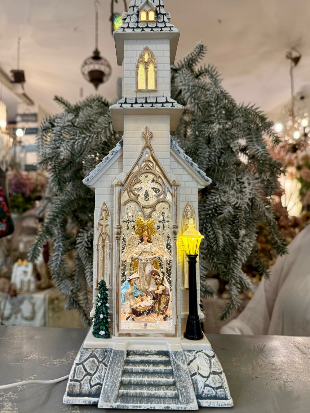 Chapelle de Noël lumineuse blanc ivoire avec clocher gothique, scène de la Nativité sous paillettes scintillantes, décoration féérique musicale pour intérieur de charme