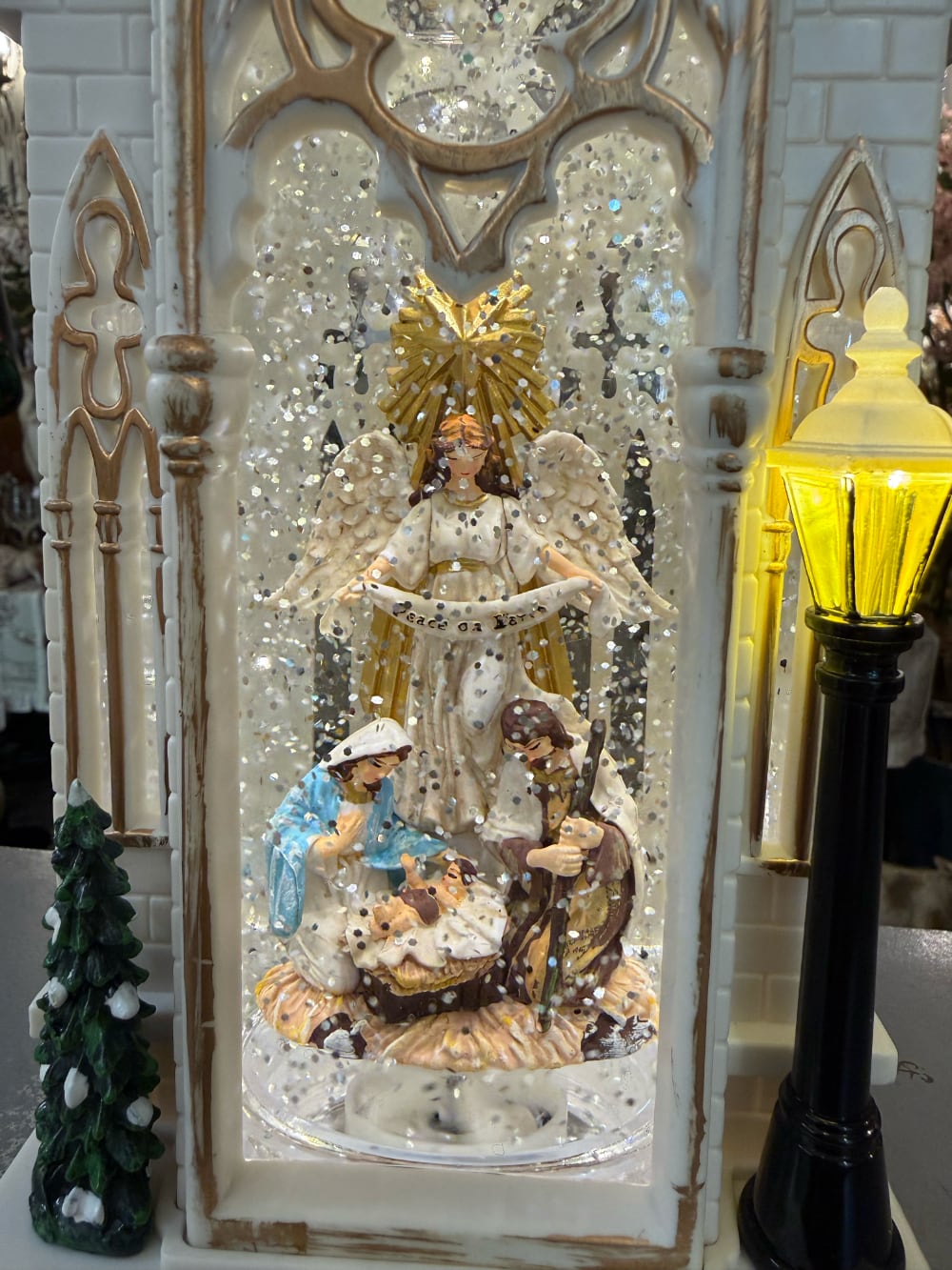 Chapelle de Noël lumineuse blanc ivoire avec clocher gothique, scène de la Nativité sous paillettes scintillantes, décoration féérique musicale pour intérieur de charme