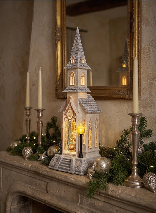Chapelle de Noël lumineuse blanc ivoire avec clocher gothique, scène de la Nativité sous paillettes scintillantes, décoration féérique musicale pour intérieur de charme