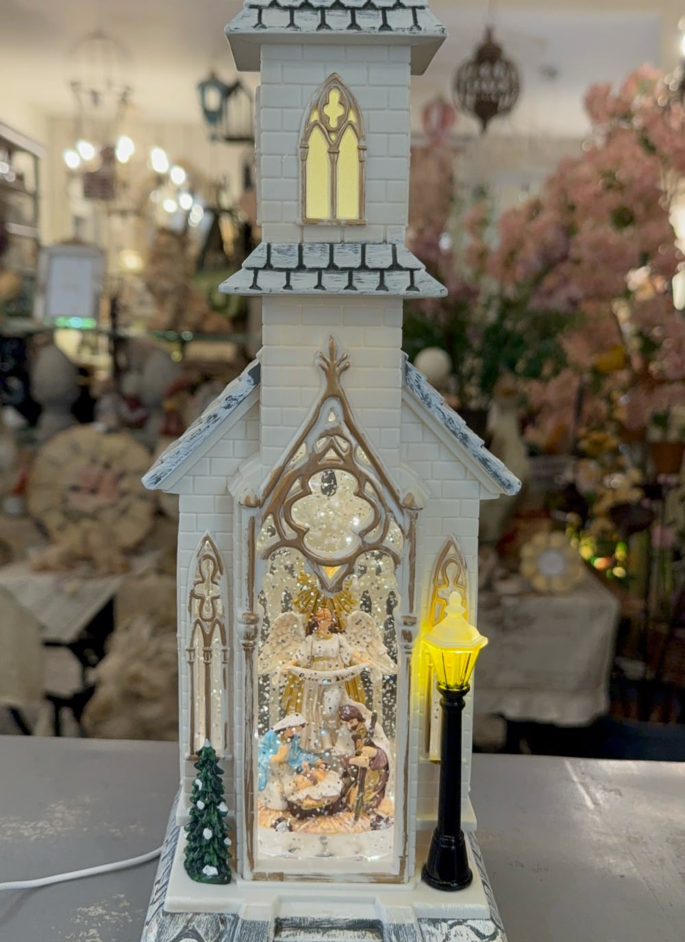 Chapelle de Noël lumineuse blanc ivoire avec clocher gothique, scène de la Nativité sous paillettes scintillantes, décoration féérique musicale pour intérieur de charme