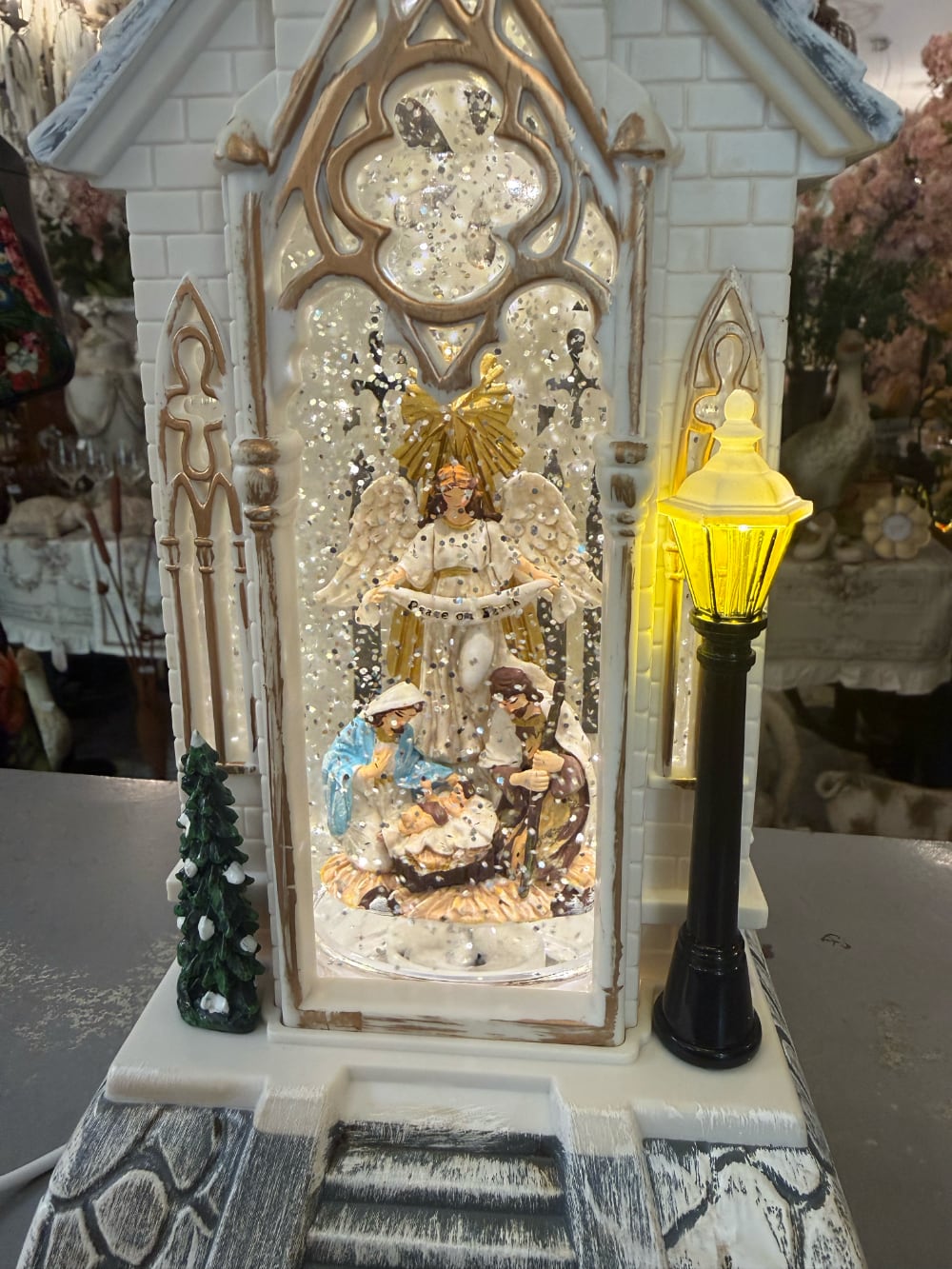 Chapelle de Noël lumineuse blanc ivoire avec clocher gothique, scène de la Nativité sous paillettes scintillantes, décoration féérique musicale pour intérieur de charme