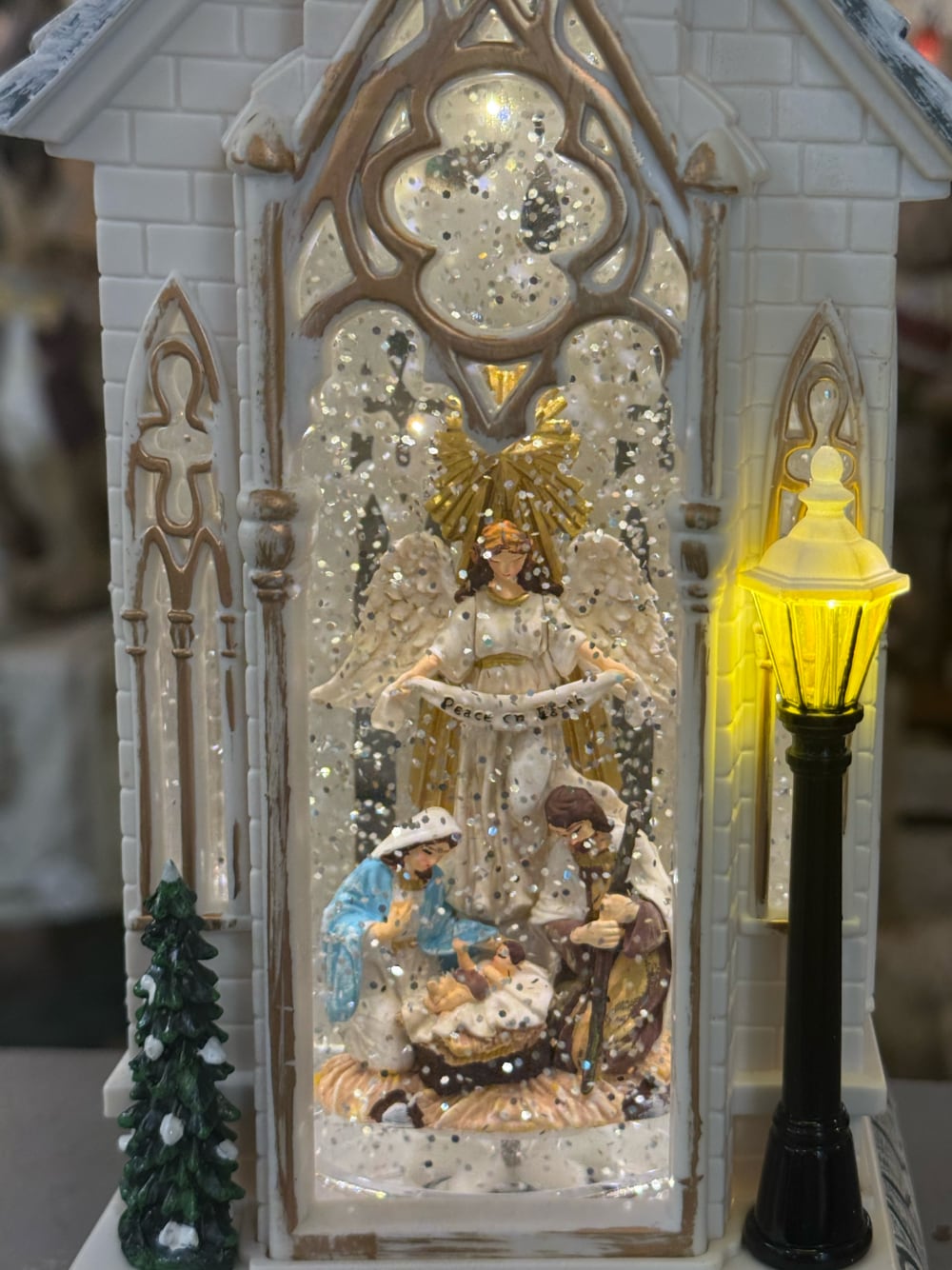 Chapelle de Noël lumineuse blanc ivoire avec clocher gothique, scène de la Nativité sous paillettes scintillantes, décoration féérique musicale pour intérieur de charme
