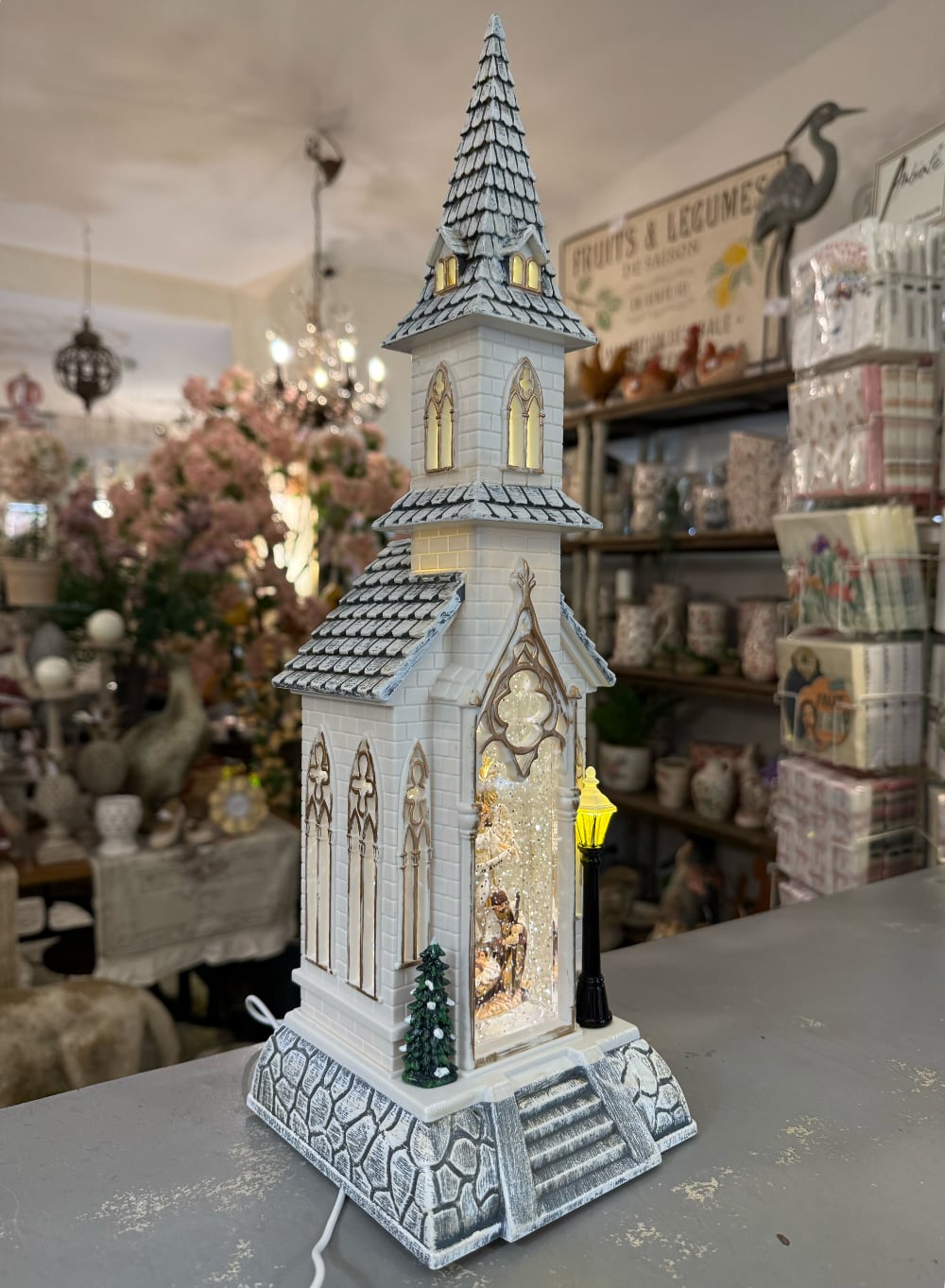 Chapelle de Noël lumineuse blanc ivoire avec clocher gothique, scène de la Nativité sous paillettes scintillantes, décoration féérique musicale pour intérieur de charme