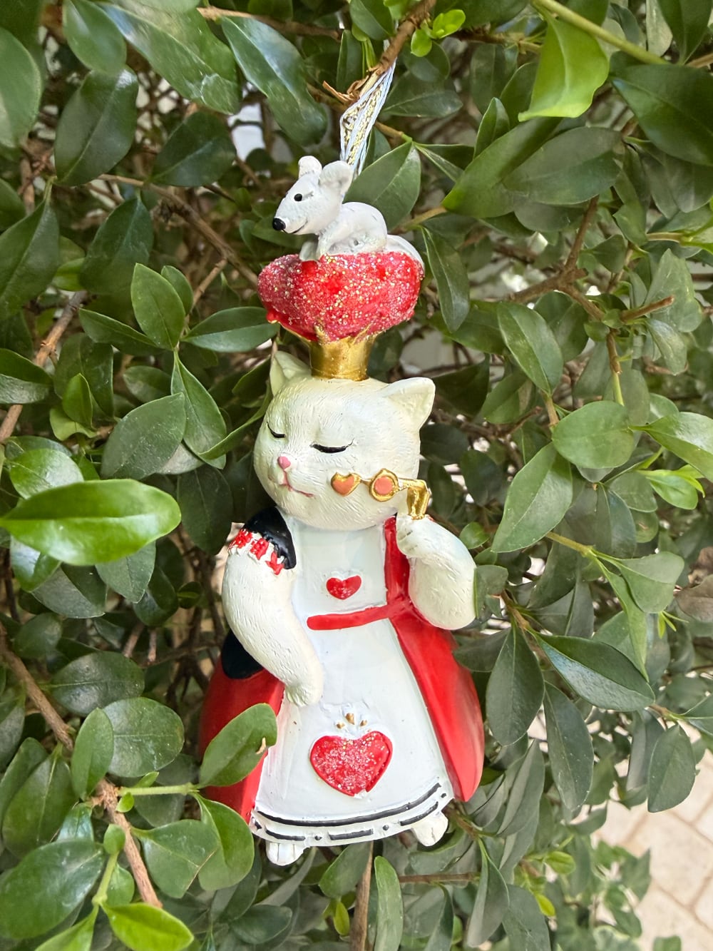 Chat d'Alice suspendu portant une robe rouge avec cœurs, une couronne dorée surmontée d'une souris et un face-à-main en forme de cœur, décoration féérique à suspendre
