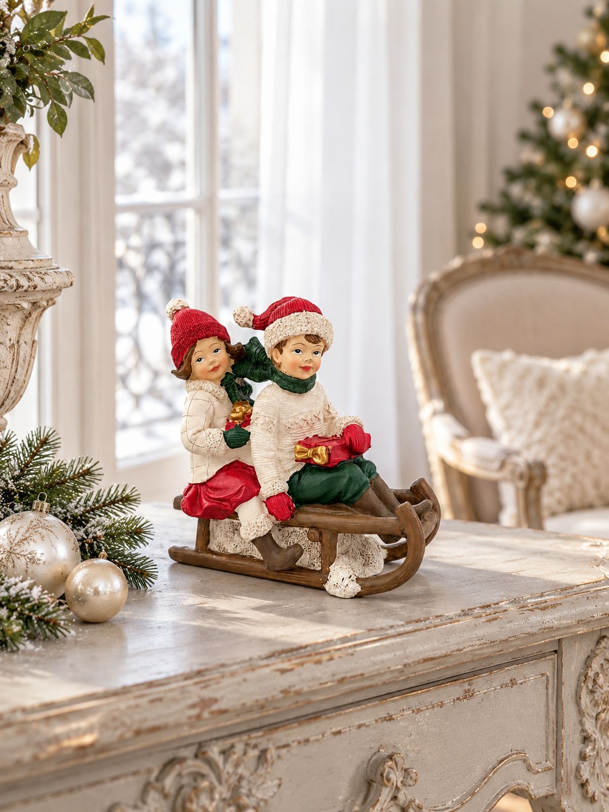 Figurine Chérubins sur une luge sur une console patinée près d’une fenêtre, avec des boules de Noël nacrées.